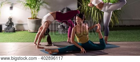Panoramic Group of asian women in sportswear pants practicing yoga in their apratment with distance in background of cityscape illumination night. Work out fitness healthy lifestyle concept