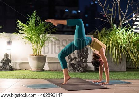 Asian female woman in sportswear bra pants practicing yoga during city lockdown alone in her apratment with background of cityscape illumination at night. Work out fitness healthy lifestyle concept.