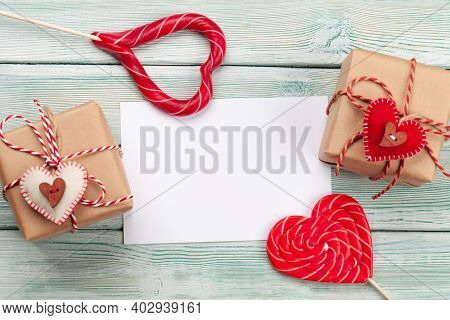 Valentines day greeting card template. Gift boxes and heart candy sweets over wooden background. Top view flat lay with copy space