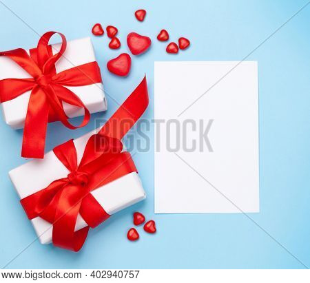 Valentines day greeting card template. Gift boxes and heart candy sweets over blue background. Top view flat lay with copy space