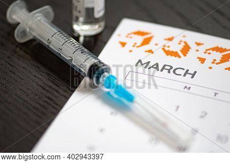 Syringe, Vial And Calendar With Month Of March On A Black Table Ready To Be Used. Covid Or Coronavir