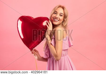 All You Need Is Love. Cheerful Blonde Woman With Red Heart Shaped Balloon Smiling And Looking At Cam