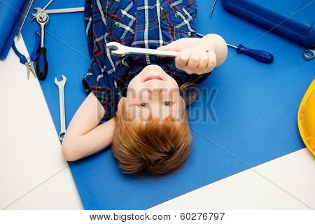 Funny little mechanic boy with wrench tools lying on a blueprint 
