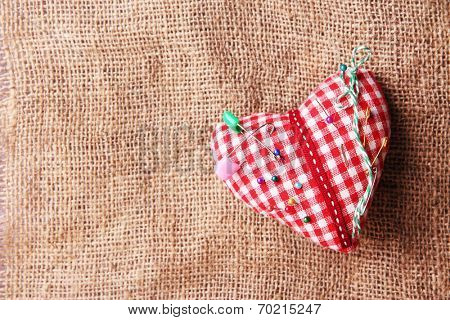 Fabric heart with color pins on sackcloth background