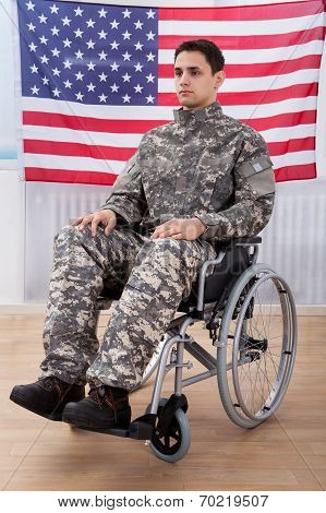 Patriotic Soldier Sitting On Wheel Chair Against American Flag