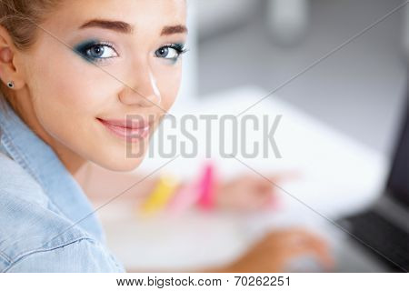 Portrait of young woman sitting on the desk with laptop in offi
