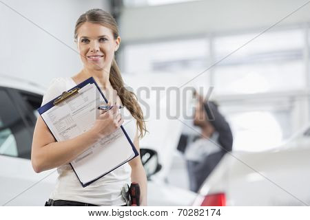 Portrait of smiling female repair worker with clipboard in car workshop