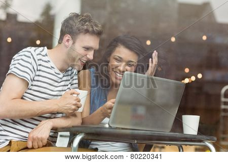 Smiling friends with a hot drink using laptop in cafe at the university