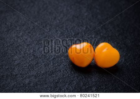 Two orange heart shaped pills or candy on grunge black slate background. Copy space.
