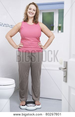 Happy Woman Weighing Herself On Scales In Bathroom