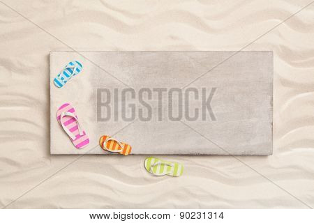 Summer background with a wooden sign and bathing shoes in the sand.
