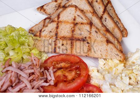 Traditional English breakfast with scrambled eggs, tomatoes, potatoes, toast and fresh salad