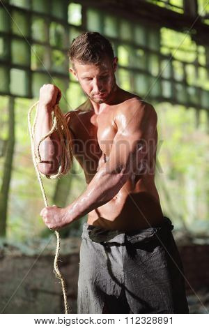 young guy in torn gray pants pulls the rope on hand in an abandoned building 