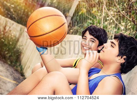 Cute basketball players sitting and resting in timeout, two teenage boys enjoying outdoor game, happy healthy active lifestyle
