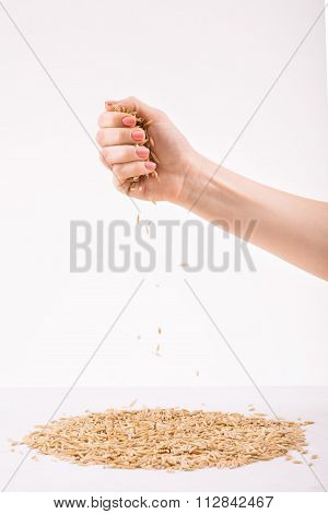 Female hand strewing wheat on the surface.