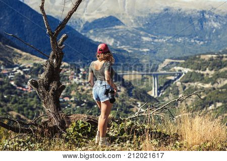 Young female photographer with professional camera near big old tree opposite greek village. A girl with camera opposite the village of Metsovo in Greece.