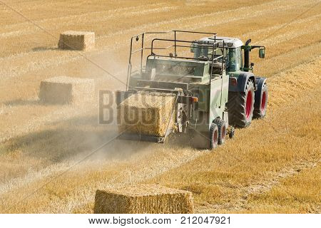 Tractor collects dry hay on the farm field and makes hay bales rear view