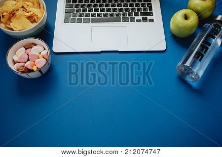 Work Space With Laptop, Candy, Chips, Water And Apple On Blue Background. Top View, Space For Text