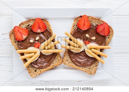 Children's breakfast with sandwiches and milk. Funny cats face sandwiches with berry chocolate banana nuts. Top view