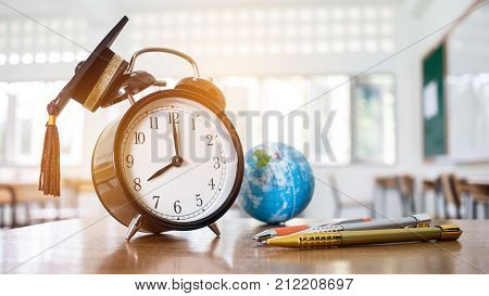 Retro alarm clock 2 o'clock left side on table teacher with earth global map Graduation cap pen in blur empty classroom. Time is indefinite continued progress of existence. Education exams concept.