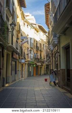 XATIVA, SPAIN, 1ST FEBRUARY 2017 - Colourful houses in a narrow street with a lady washing her porchway Xativa (Jativa) Valencia Spain