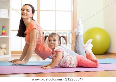 Mother and child daughter doing yoga exercises on floor in the room at home. Family having fun indoors with fitness.