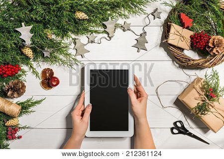 Juniper branches with a Christmas decor. Christmas, New Year background. Coniferous branches of juniper and white tablet with black screen. Top view, flat design. Christmas tree on white wooden background.