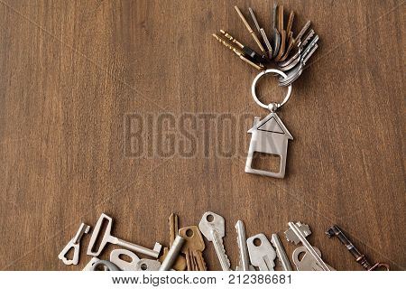 Bunch of keys with house shaped trinklet against wooden background and collection of different keys. Safety, security and real estate concept, top view, copy space