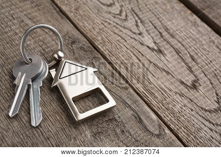 Two steel keys with house shaped trinklet on keyring on wooden background with copy space. Home key, safety, security, real estate and rent concept