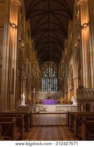 Sydney Australia - March 23 2017: Chancel with purple-dressed altar gothic tabernacle white statues and large stained window in back. Rather dark alcove like setting. Benches and pulpit in front.