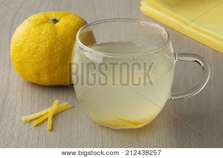 Glass cup with fresh Japanese Yuzu tea and a whole yuzu in the background
