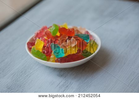 Jelly bears on wooden background. Gummy candy bears background. Colorful fruity candy bears. Jelly fruit candy on white wooden background. Bowl with gummy candy. Heap of multicolored gummy bears.