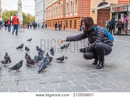 Brasov Romania October 06 2017 : Young woman feeding pigeons outdoors in the Old city of Brasov in Romania