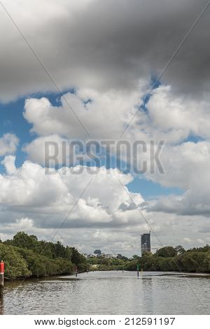 Parramatta Australia - March 24 2017: Sailing on Parramatta River the first buildings of the town peep at the horizon over a green belt under a heavy cloudscape.