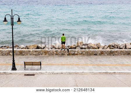 Runner on city street looking at inspiring sea view. Young athlete male training and doing workout outdoors in urban scene. Sport and fitness training inspiration and motivation. Vintage tone.