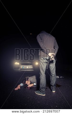 Masked murderer shooting man in suit in front of car on route