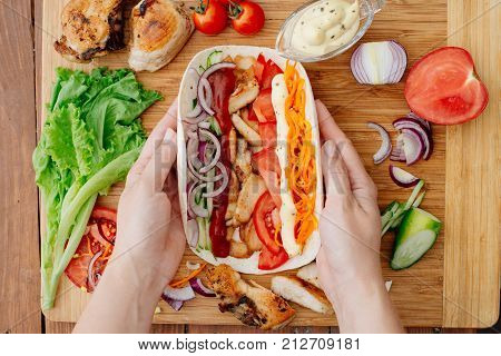 The process of preparing chiken shawarma. Ingredients sliced lie on the kitchen board. Fast food. Eastern food. Dishes of oriental cuisine lying on pita bread and decorated with greens and vegetables