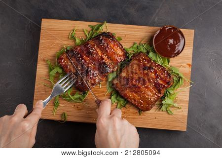 Hands Of Young Woman Cutting Delicious Pork Ribs Bbq In Kitchen. Top View