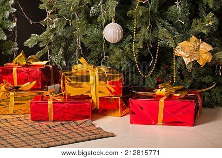 Christmas gifts lie under the tree. The boxes are wrapped in red and gold paper. Background for the holiday.