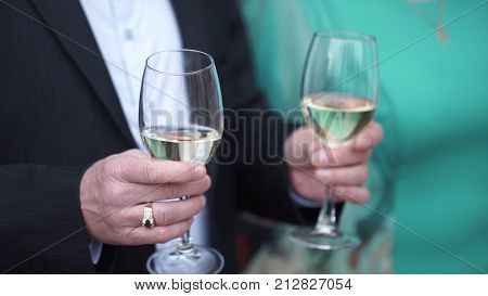 Close up of Caucasian man in black suit and white shirt holding two tall glasses with white wine. Closeup of two glasses of champagne on tray holded by handsome waiter in tuxedo. Man in suit holding 2 glasses HD