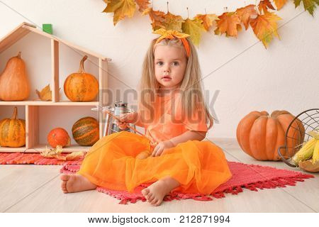 Adorable little girl with magic wand near pumpkins indoors