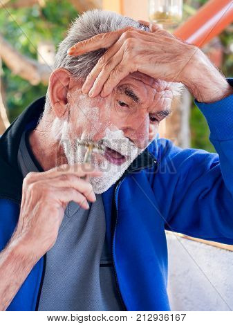 A portrate of a shaving elderly handsome man standing outside.