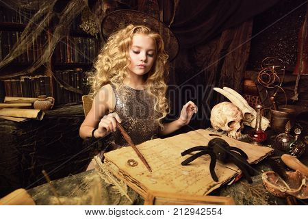 Beautiful charming little witch conjures in her lair. Halloween. 