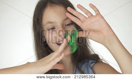 Beautiful cheerful teen girl playing with green fidget spinner on a white background
