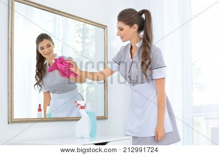 Chambermaid cleaning mirror with rag in room
