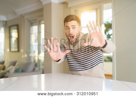 Young handsome man at home afraid and terrified with fear expression stop gesture with hands, shouting in shock. Panic concept.