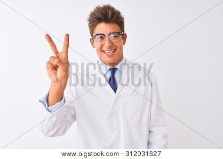 Young handsome sciencist man wearing glasses and coat over isolated white background smiling with happy face winking at the camera doing victory sign with fingers. Number two.