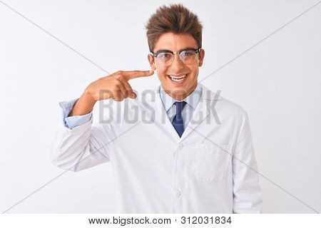 Young handsome sciencist man wearing glasses and coat over isolated white background Pointing with hand finger to face and nose, smiling cheerful. Beauty concept