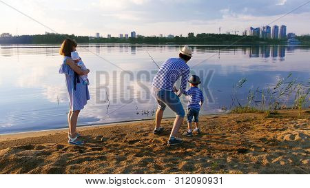Family Fishing On The Riverside At Sunset - Man With His Wife And Two Chidlren