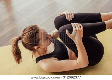 From Above Slim Lady In Black Sportswear Doing Pavanamuktasana Exercise On Gym Floor During Yoga Tra